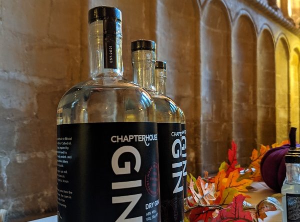 Chapterhouse Gin Bristol Cathedral bottle stands on a table decorated by autumn leaves with the chapter house of the cathedral in the background