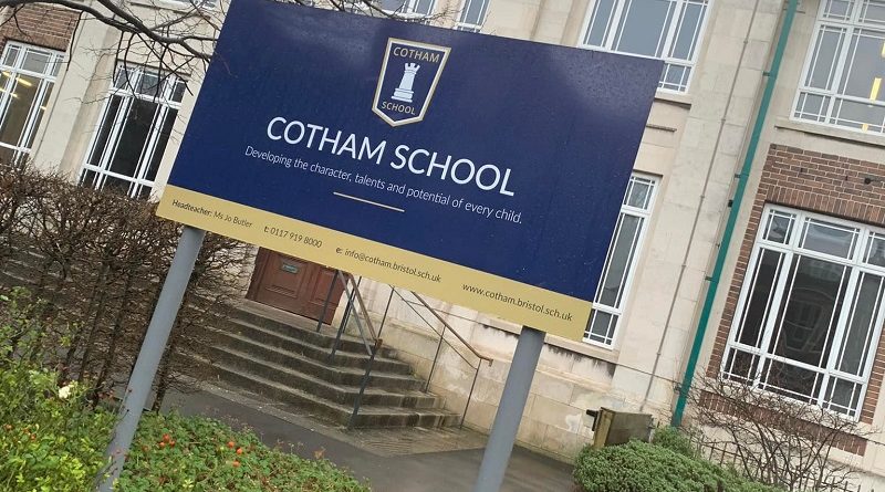 Photo of the front of Cotham School. An imposing looking building in the back. In the front is a blue school sign saying 'Cotham School'.