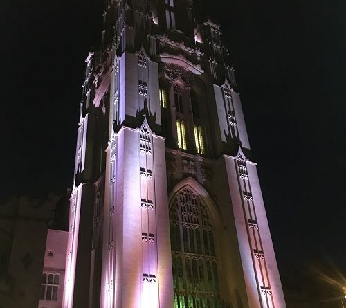 Bristol University Tower Tours. A photo of the Wills Memorial Tower at night lit up in purple lighting